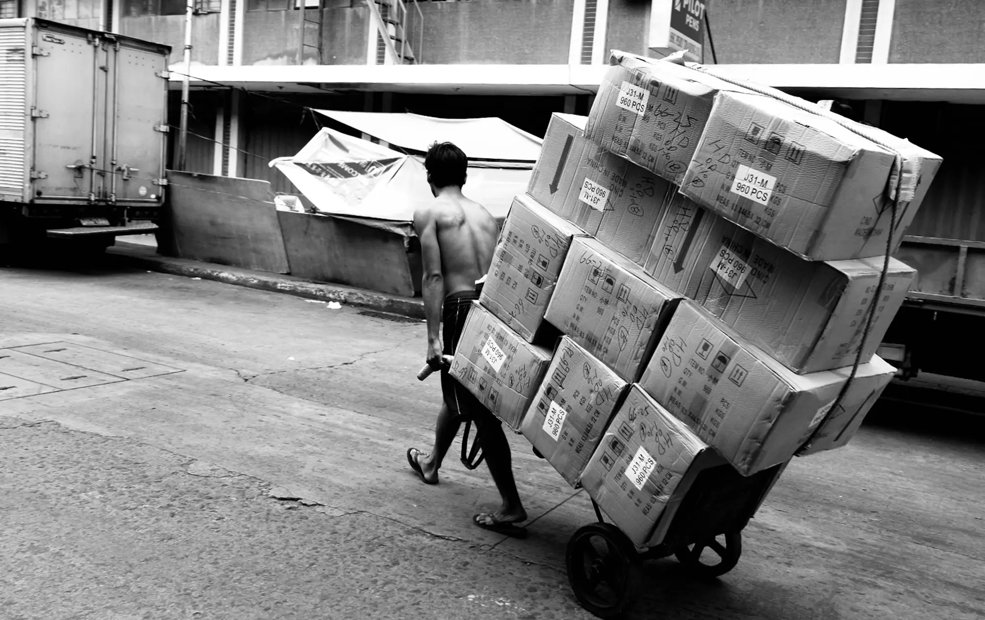 Man pushing a trolley stacked with boxes down a city street