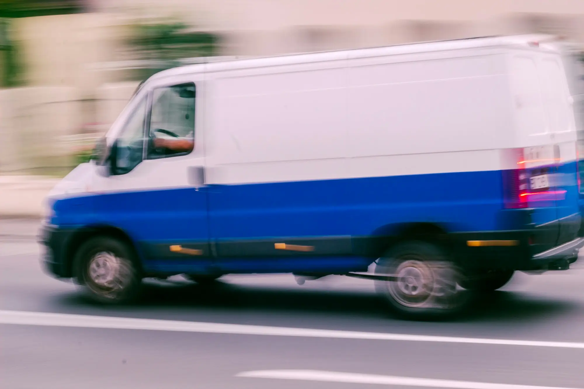Blue and white van driving down a city street on a delivery run