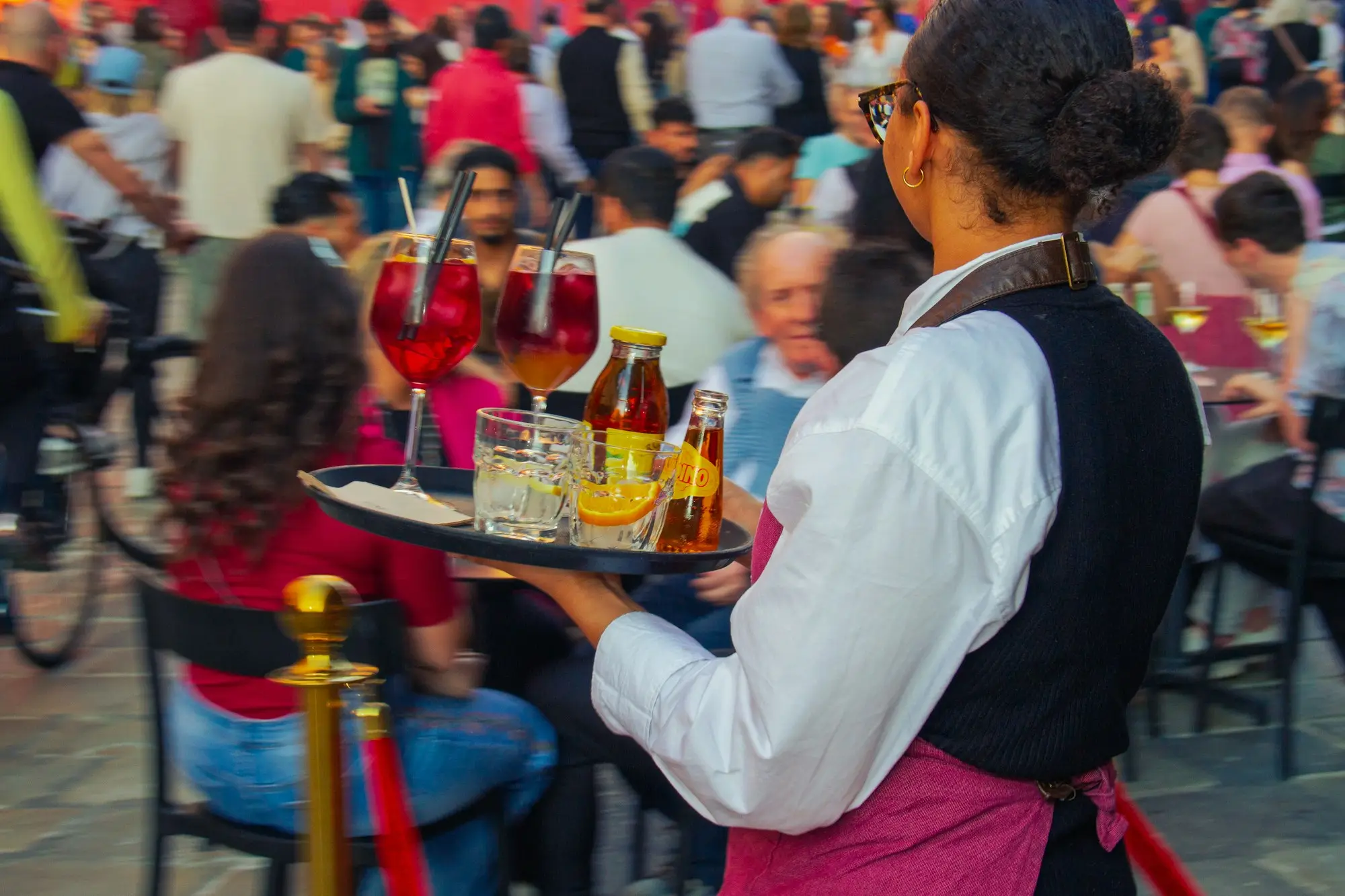 Server carrying a tray of drinks and bottles through a busy venue